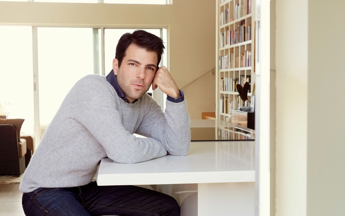 Zachary Quinto sitting at a counter with bookshelves