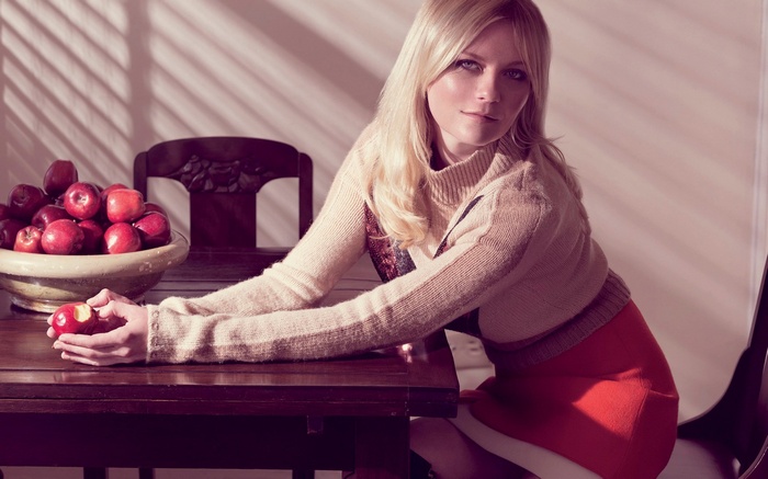 Kirsten Dunst sitting at a table with apples
