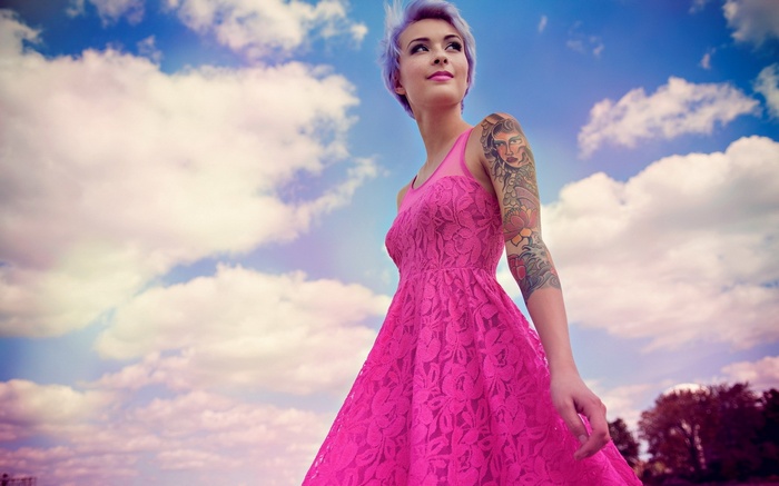 Woman with tattoos in a pink dress against a cloudy sky