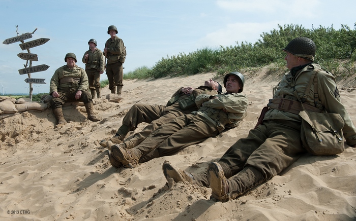 Soldiers resting on a sandy dune with directional signs