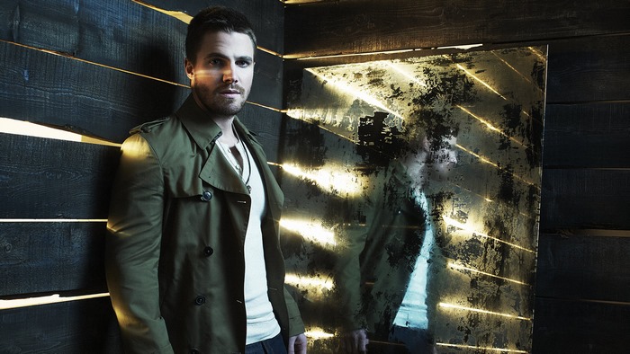 Stephen Amell leans against a wooden wall