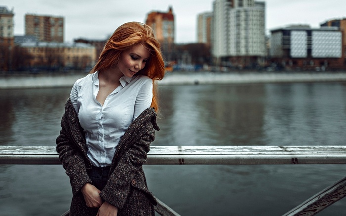 Woman with red hair by a river in a city