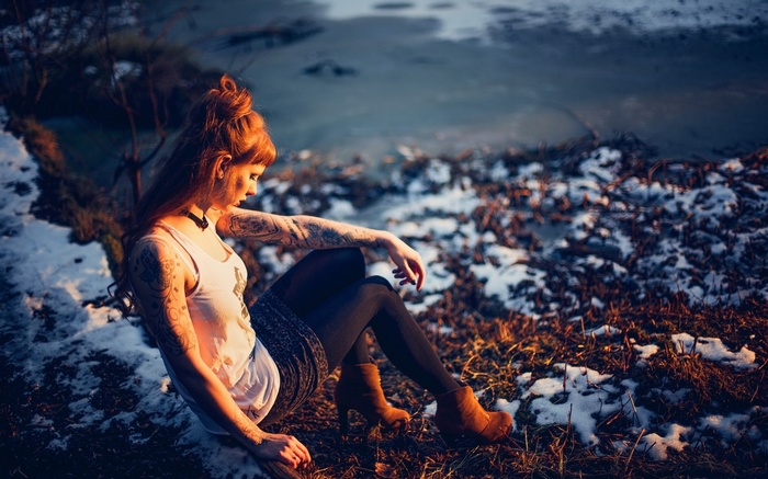 Woman with tattoos sitting by a frozen body of water