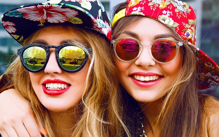 Two young women wearing floral hats and sunglasses