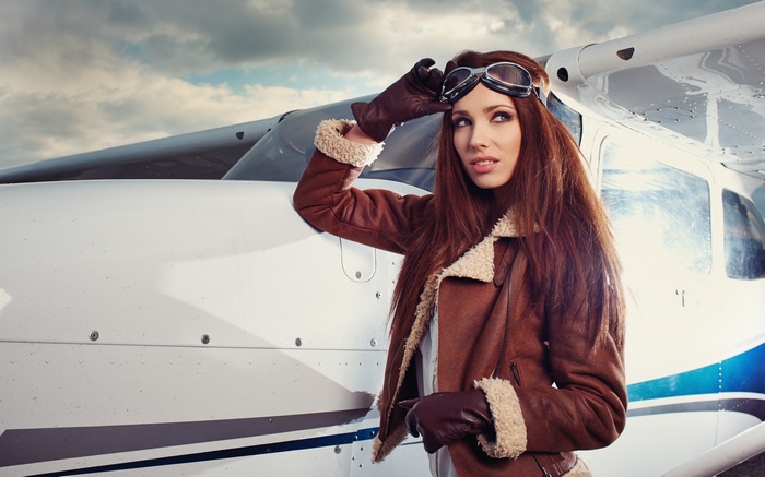 Woman in aviator jacket and goggles by airplane