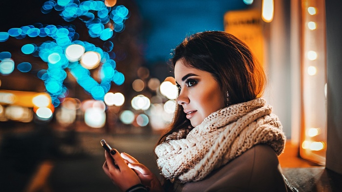 Woman looking at phone with bokeh lights