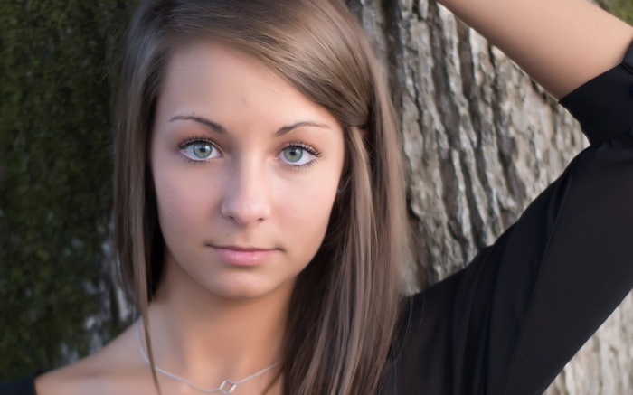 Young woman with blue eyes leaning against a tree