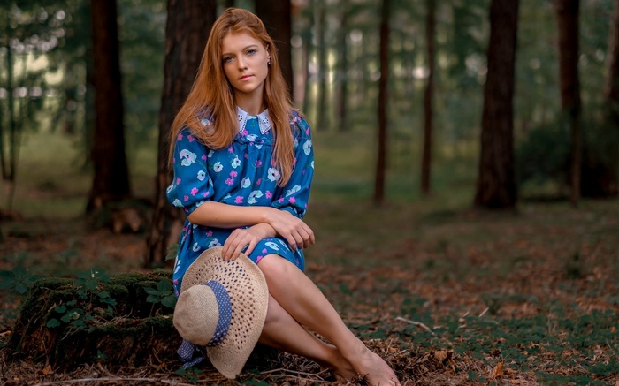 Young woman with red hair in a blue dress holding a hat