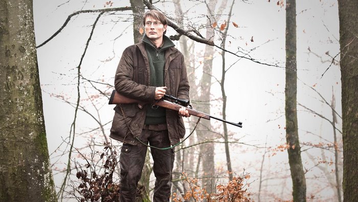 Mads Mikkelsen with a rifle in a forest