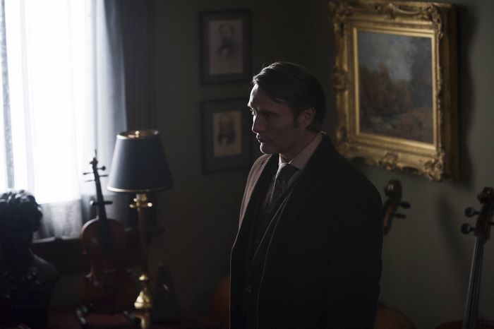 Mads Mikkelsen in a dark room with paintings and violins