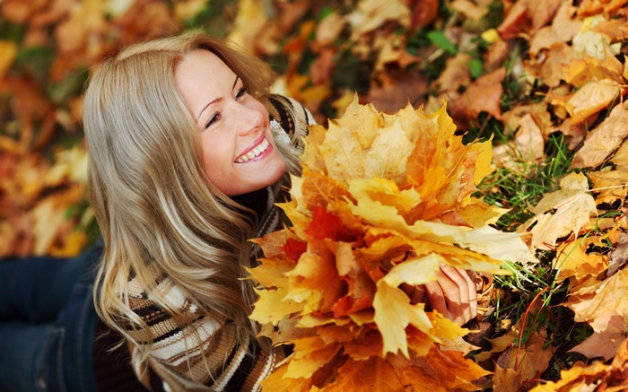 Woman lying in autumn leaves holding maple leaves