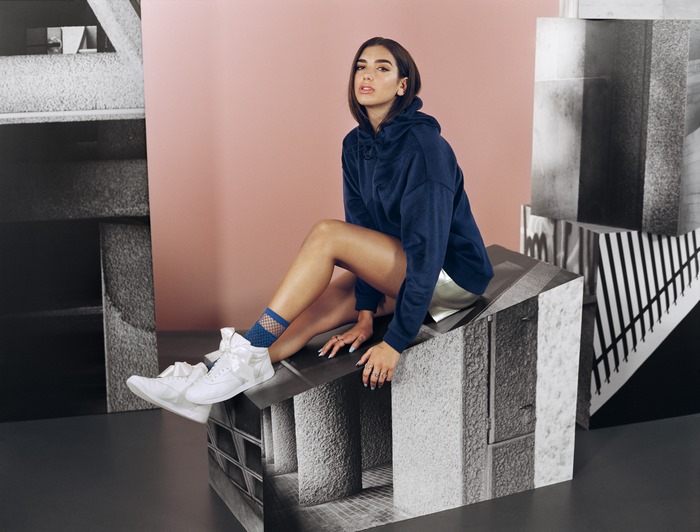 Dua Lipa sitting on a geometric structure