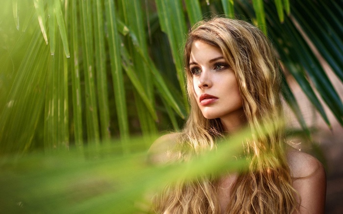 Woman with blonde hair among palm leaves