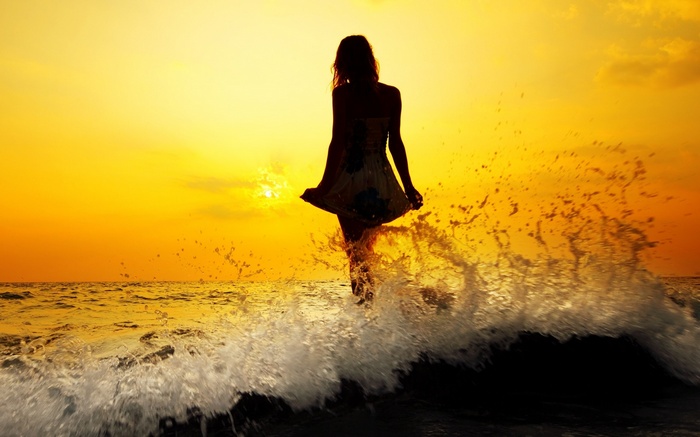 Woman in dress walking through ocean waves at sunset
