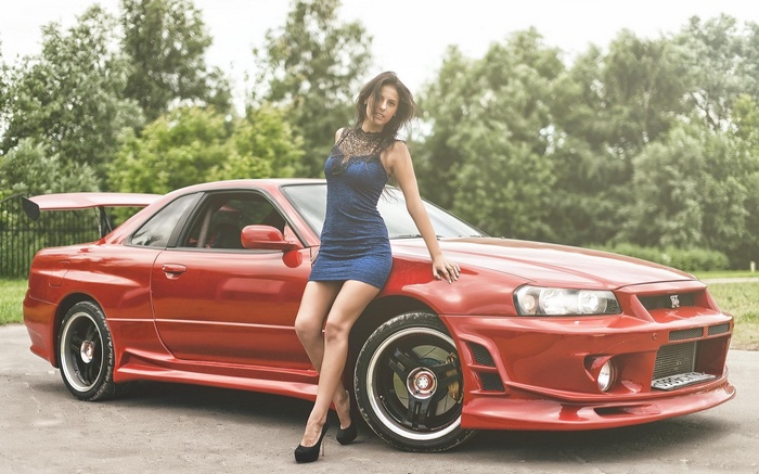Woman in blue dress leaning on red sports car