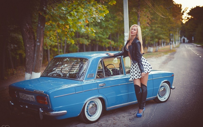 Woman in polka dot skirt and leather jacket leaning on blue car