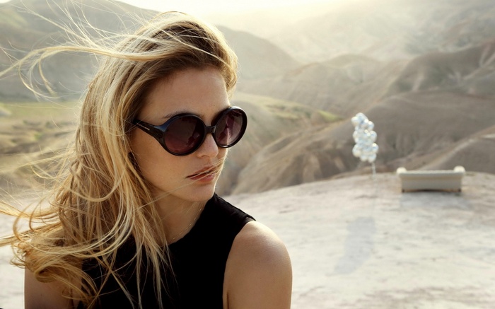 Woman with sunglasses in a desert landscape with balloons and a couch