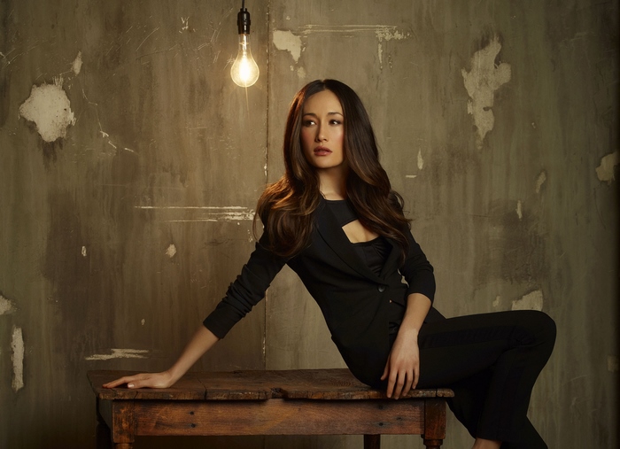 Maggie Q sitting on a wooden table