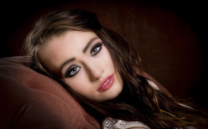 Woman with dark hair and makeup lying on a pillow