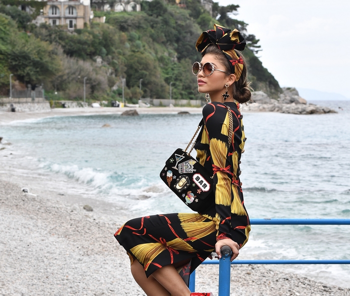 Zendaya on a beach with a patterned dress and handbag