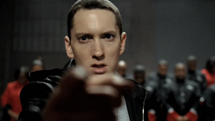 Eminem in a dark room with people behind him