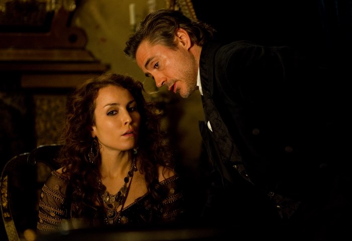 Noomi Rapace in a dark, ornate room