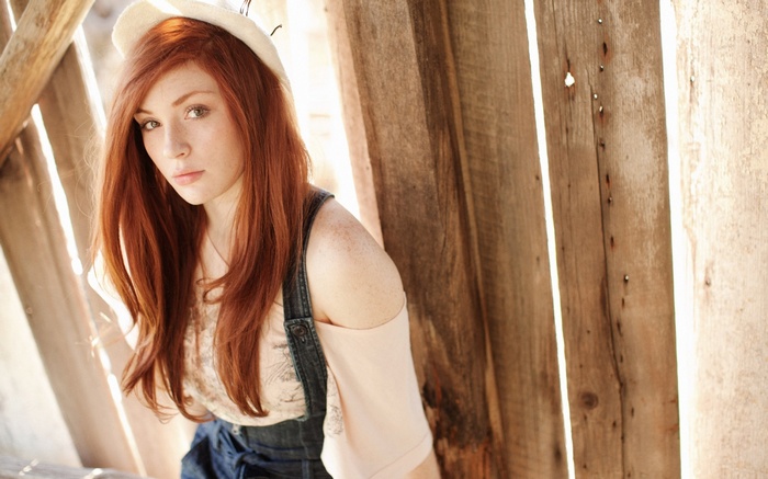 Red-haired woman wearing a hat and overalls