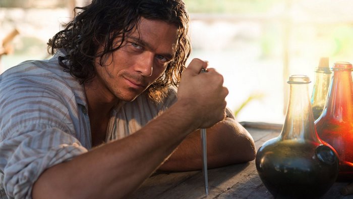 Luke Arnold in a striped shirt holding a knife