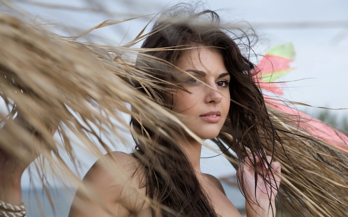 Woman with long brown hair behind dry palm leaves