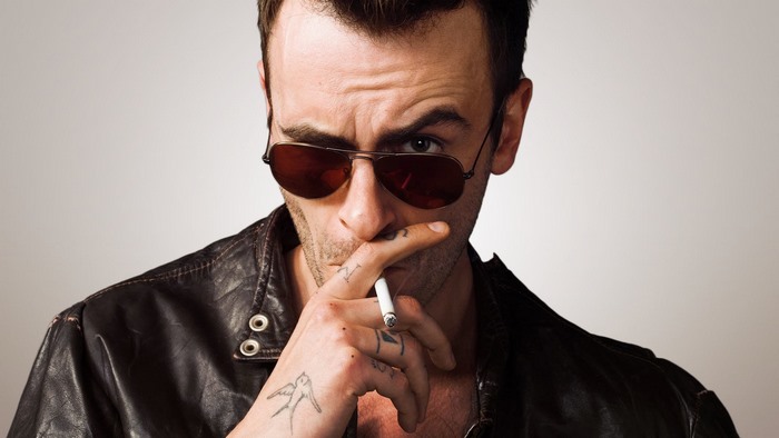 Joseph Gilgun wearing sunglasses and leather jacket smoking