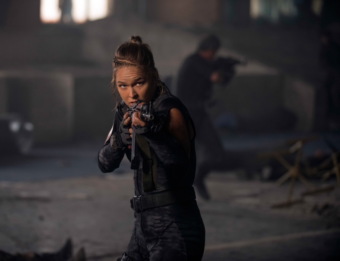 Ronda Rousey aiming a rifle
