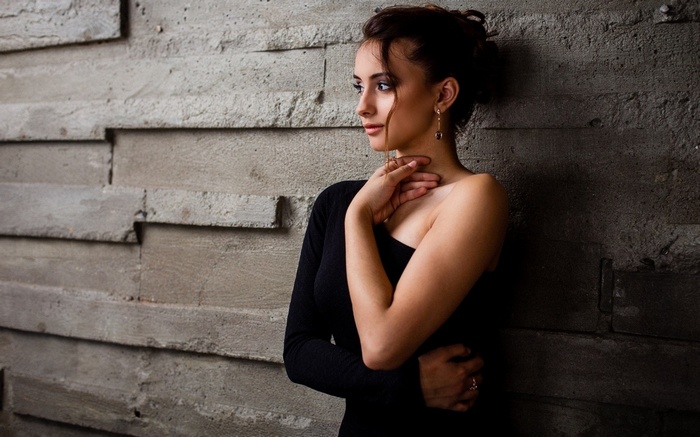 Woman in black dress leaning against a textured wall