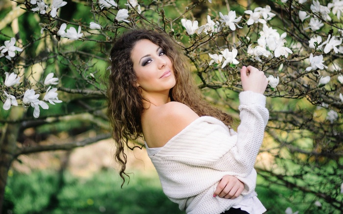 Woman in a white sweater with curly hair near white flowers