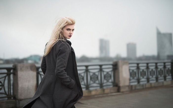 Woman in coat on a bridge with city skyline