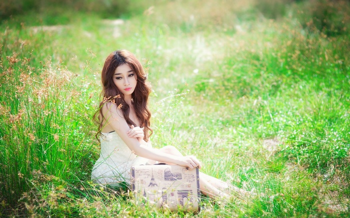 Woman sitting in a grassy field with a suitcase