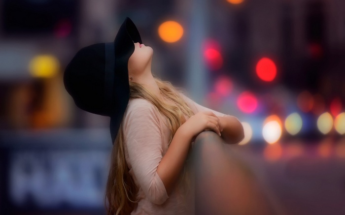 Girl in a hat looking up at bokeh lights