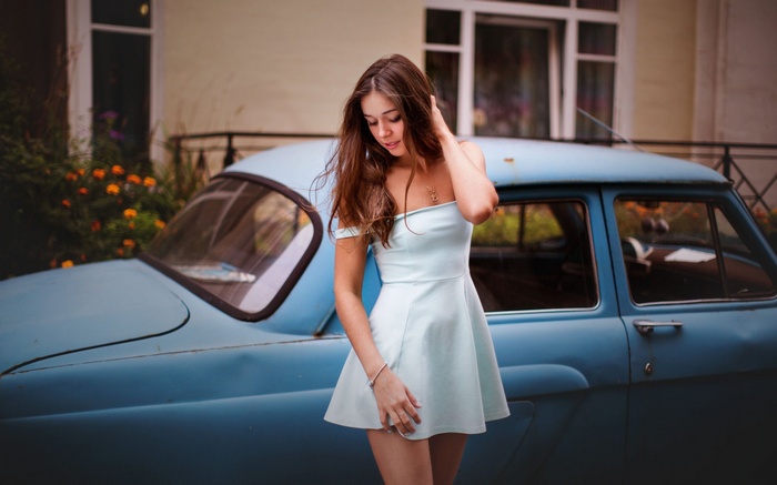 Woman in a light blue dress posing by a vintage blue car