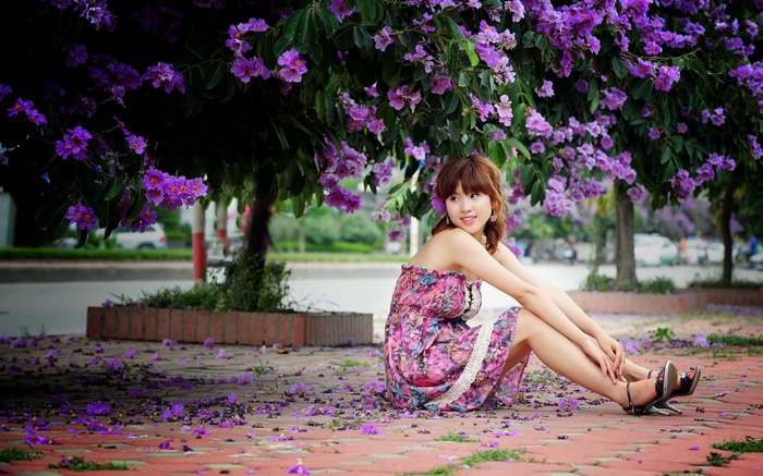 Woman in floral dress sitting under purple flowers