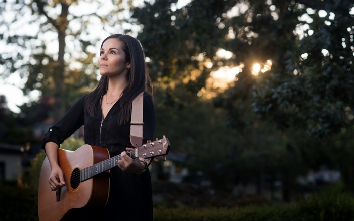 Woman playing acoustic guitar outdoors at sunset