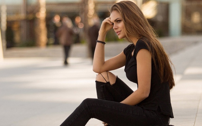 Woman in black shirt and ripped jeans sitting outdoors