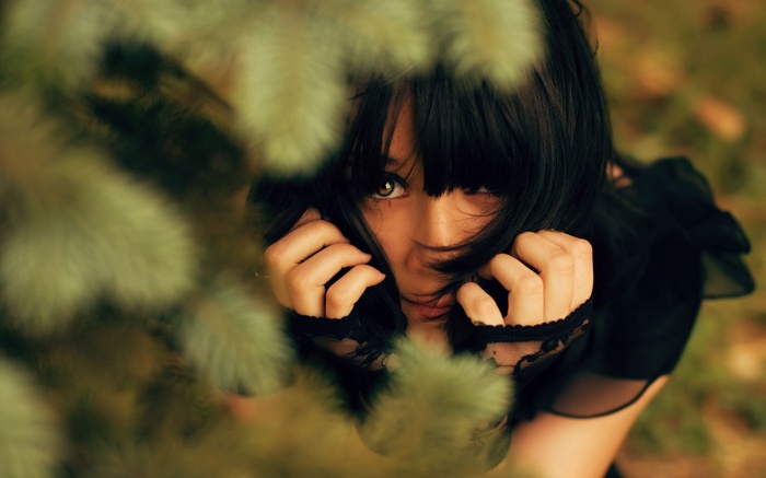 Woman peeking through pine branches