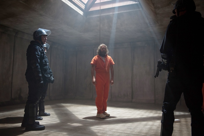 Kevin Costner in an orange jumpsuit with guards