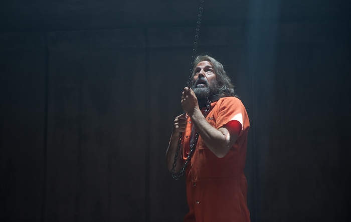 Kevin Costner in orange jumpsuit with chain