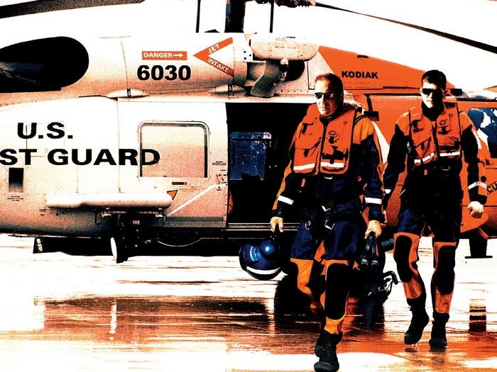 Two U.S. Coast Guard members walk by a helicopter