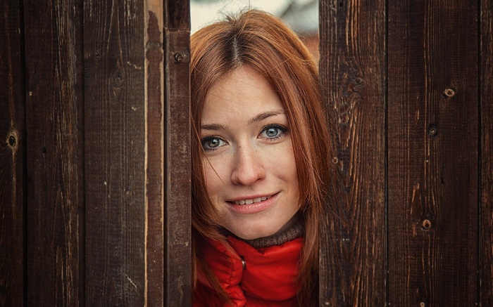Woman with red hair peeking through wooden fence