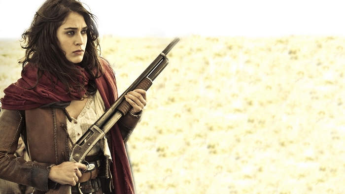 Lizzy Caplan holding a shotgun in a field