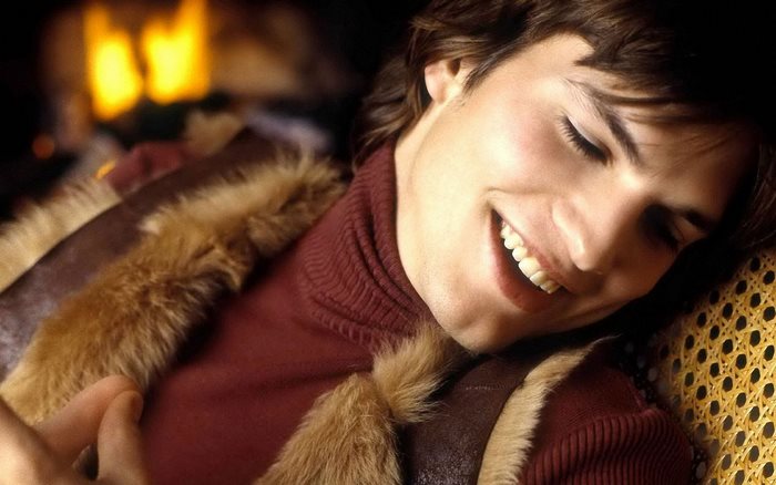 Ashton Kutcher smiling by a fireplace