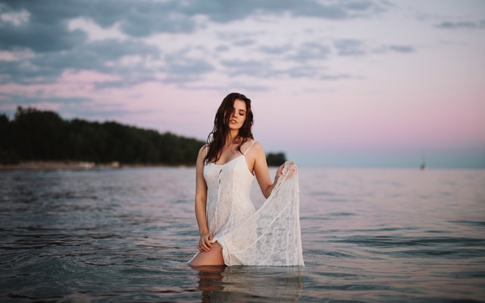 Woman in white dress standing in water at sunset
