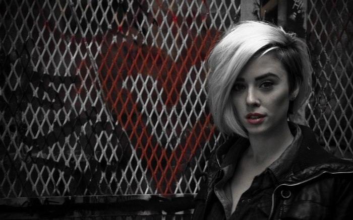 Woman with blonde hair in front of a metal fence