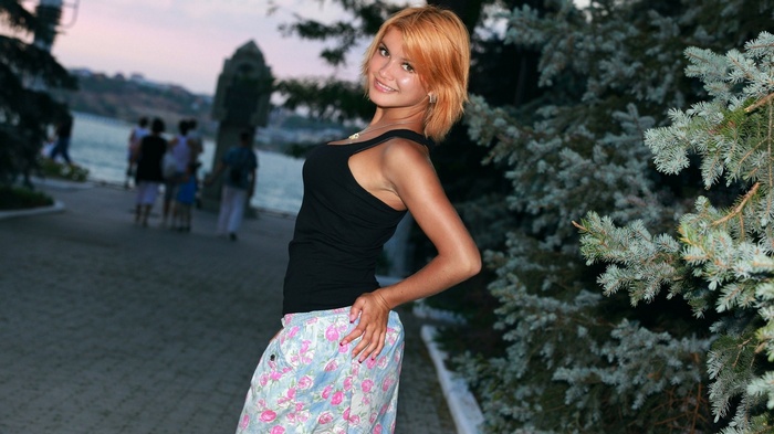 Woman in black tank top and floral pants posing outdoors